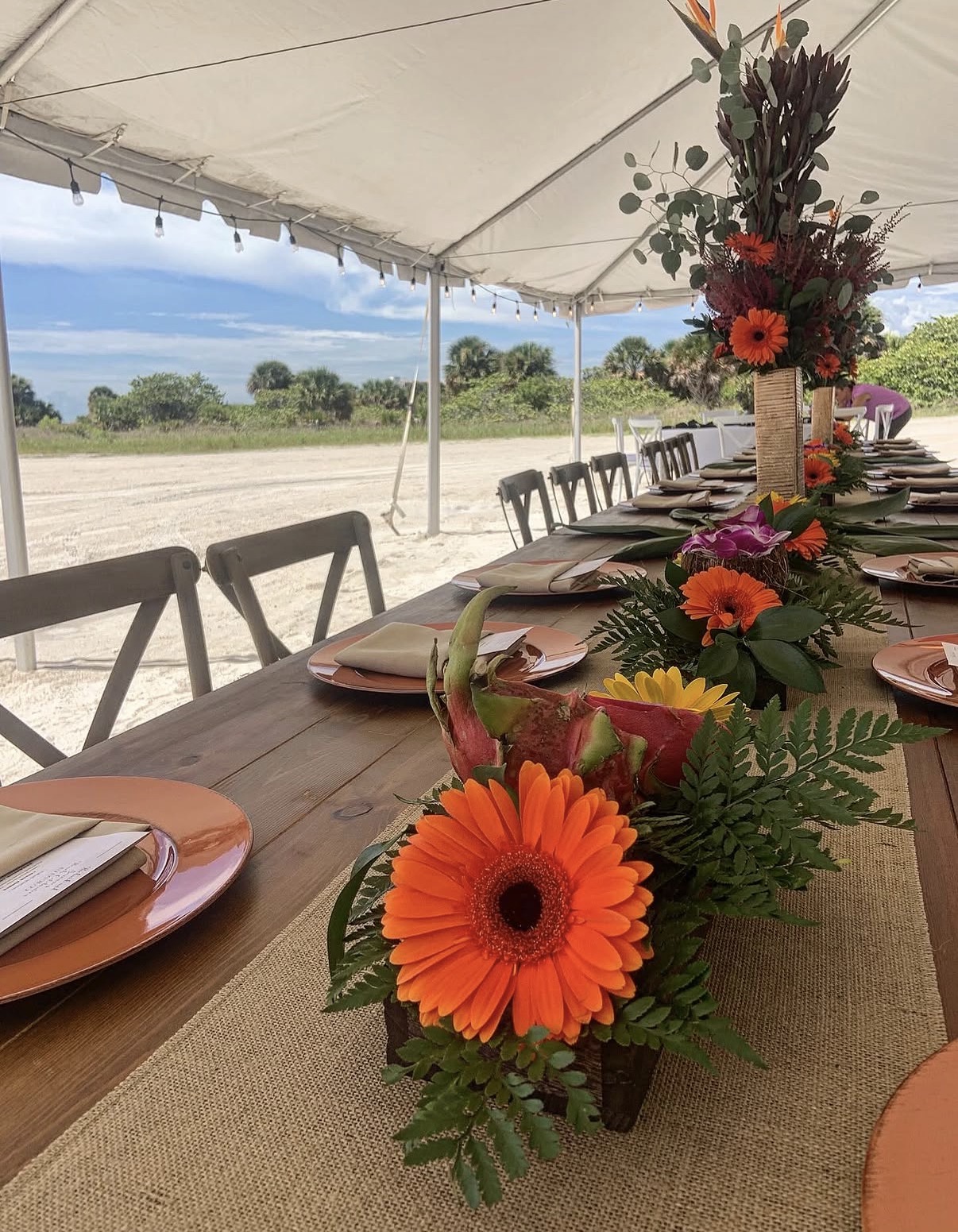 Outdoor tented reception with orange floral centerpieces along a long farm table.